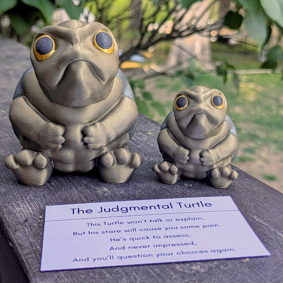 Large and small Judgmental Turtle™ figurines next to product description card on wood surface.