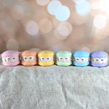 A lineup of six pastel macaron frogs in pink, orange, yellow, green, blue, and purple on a neutral background.