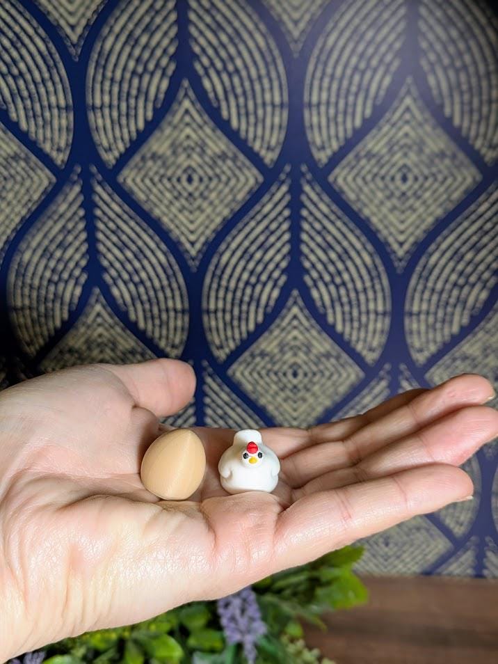 Tiny brown egg and miniature chicken figurine shown resting in an open palm, highlighting their small size.