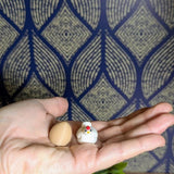 Tiny brown egg and miniature chicken figurine shown resting in an open palm, highlighting their small size.