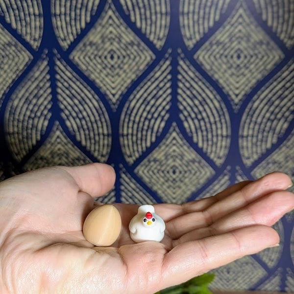Tiny brown egg and miniature chicken figurine shown resting in an open palm, highlighting their small size.