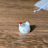 Close-up of a tiny white chicken game piece with a red comb, placed on a wood-textured game board.
