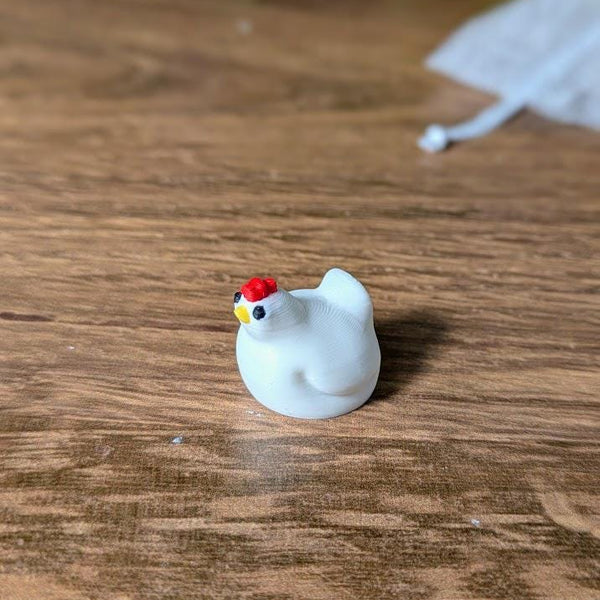 Close-up of a tiny white chicken game piece with a red comb, placed on a wood-textured game board.