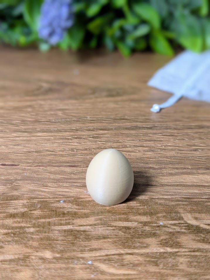 Small, smooth egg-shaped game piece sitting on a rustic wooden surface with a blurred background.