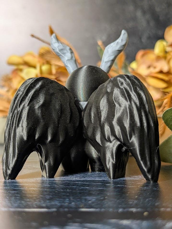 Back view of Mothman showing detailed wings and curled antennae, framed by golden fall foliage.