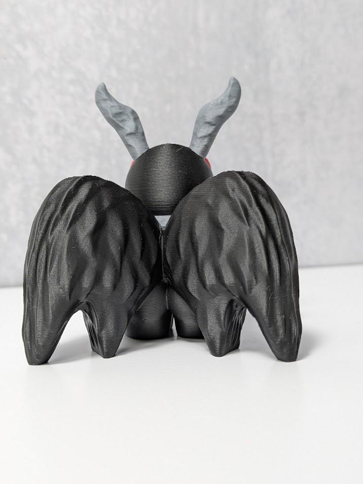 Back view of Mothman figurine with black textured wings and curled gray antennae.