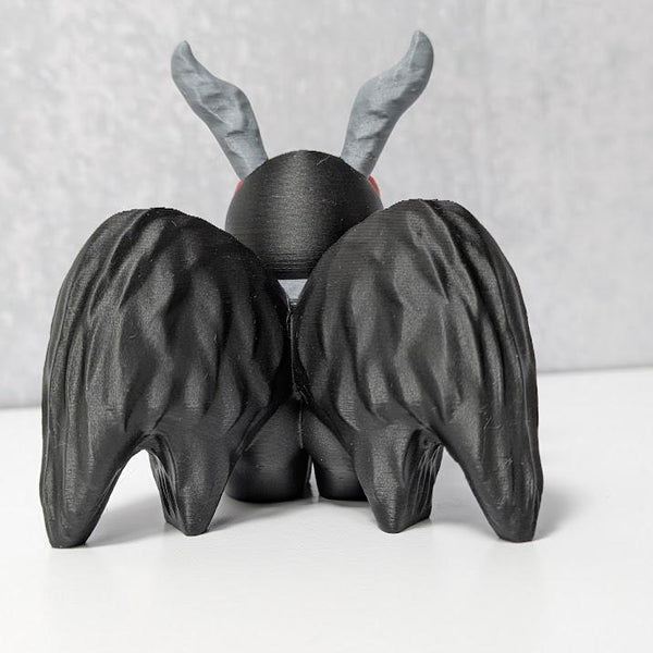 Back view of Mothman figurine with black textured wings and curled gray antennae.