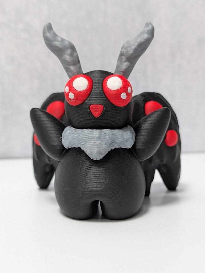 Front view of Mothman figurine with six red eyes, raised arms, and dramatic black wings.