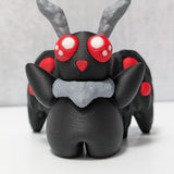 Front view of Mothman figurine with six red eyes, raised arms, and dramatic black wings.
