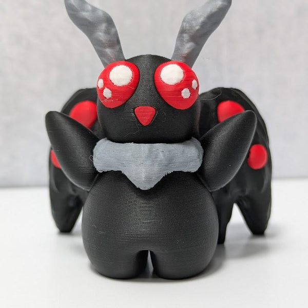 Front view of Mothman figurine with six red eyes, raised arms, and dramatic black wings.