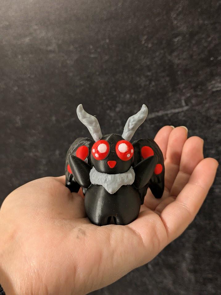Mothman figurine with red eyes held in hand for scale, against a dark textured background.