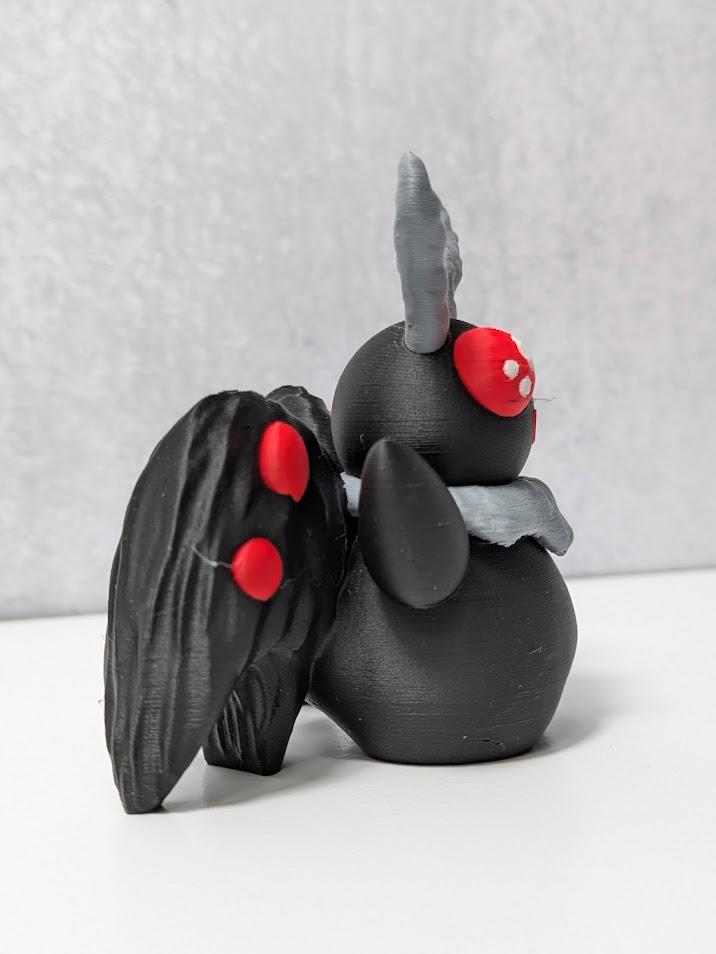 Side view of Mothman figurine with black textured wings and curled gray antennae.