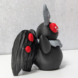Side view of Mothman figurine with black textured wings and curled gray antennae.