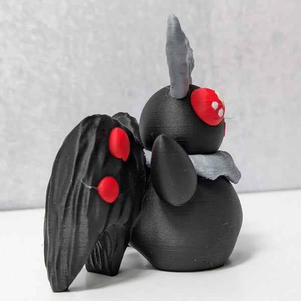 Side view of Mothman figurine with black textured wings and curled gray antennae.