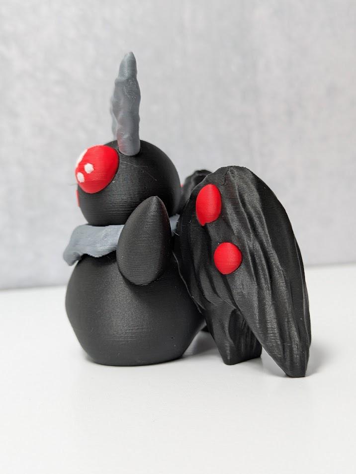 Angled view of Mothman with glowing red eyes, sculpted black body, and folded wings.