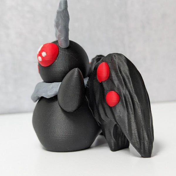 Angled view of Mothman with glowing red eyes, sculpted black body, and folded wings.