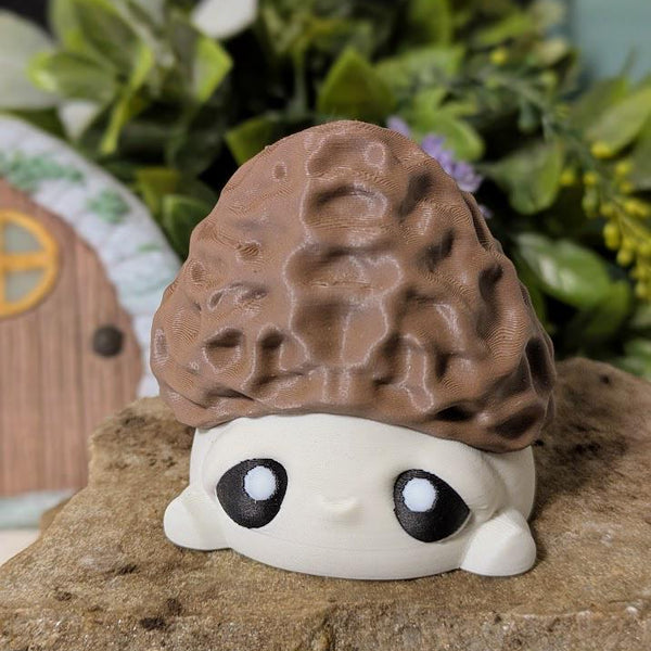 Front view of wide-eyed mushroom goblin with morel-style cap, sitting on stone with fairy door in background.