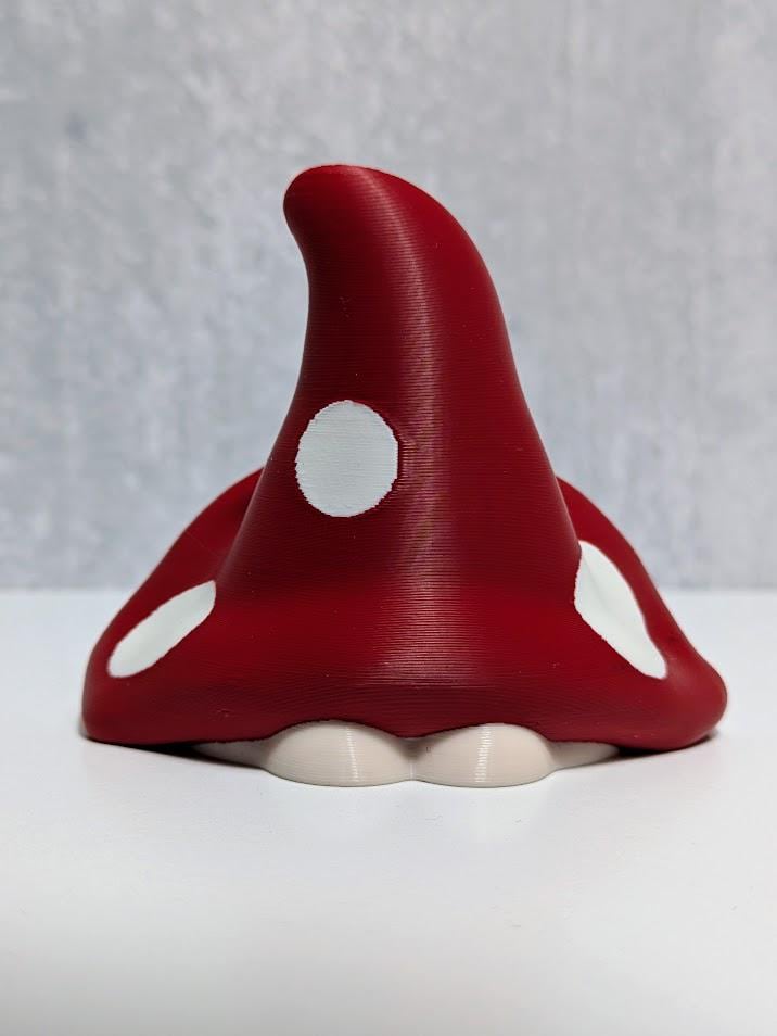 Back view of red mushroom goblin showing curved cap with white spots and small white base.