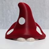 Back view of red mushroom goblin showing curved cap with white spots and small white base.