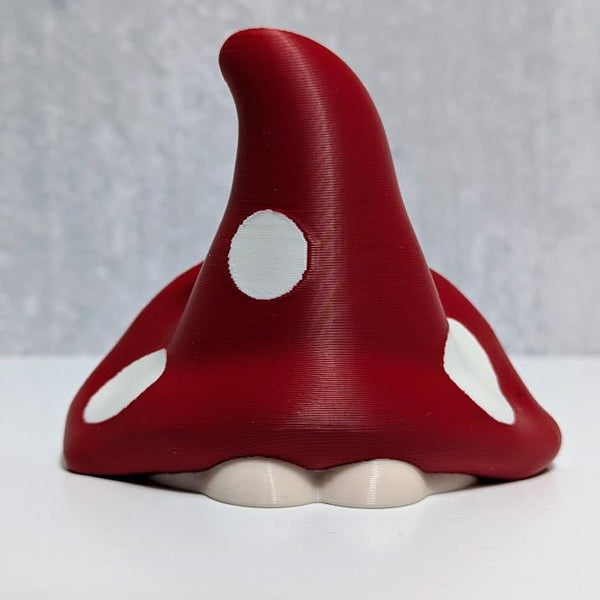 Back view of red mushroom goblin showing curved cap with white spots and small white base.