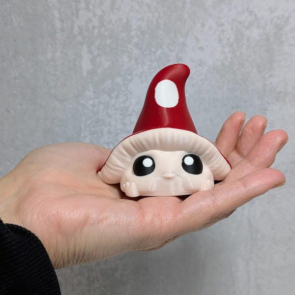 Red-capped mushroom goblin with wide eyes resting in an open hand for size reference, against gray background.