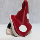 Side view of red-capped mushroom goblin with large white spots, partially hiding behind its oversized hat.