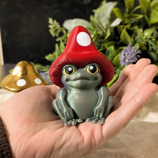 Mushroom frog figurine held in a hand for scale, with cozy warm lighting and florals in the background.