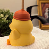 Side view of duck figurine wearing a red plunger hat, perched on a towel in front of a bathroom faucet.