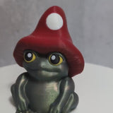 Video of a green frog figurine wearing a red mushroom hat.