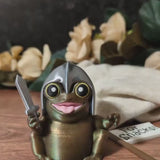 Video showing a rotating view of Sir Glorb™, a tiny frog knight figurine with a sword and removable battle flag that says “For Snacks!”