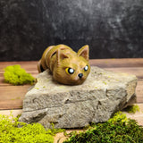 A 3D printed Snat figurine — a flexible, poseable snake-cat hybrid — is shown moving and curling in different positions. The golden brown PLA sparkles under the light while the cat face maintains a stern expression. The articulation of each segment allows the Snat to wrap around objects, coil, and uncoil with fluid motion.