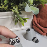 A short video clip of a chunky raccoon figurine getting gently poked, clearly unbothered and full of snacks.