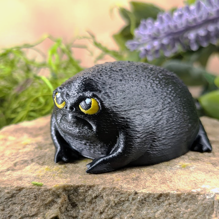 Left side view of the angry black frog figurine, highlighting its rotund shape and subtle leg definition.