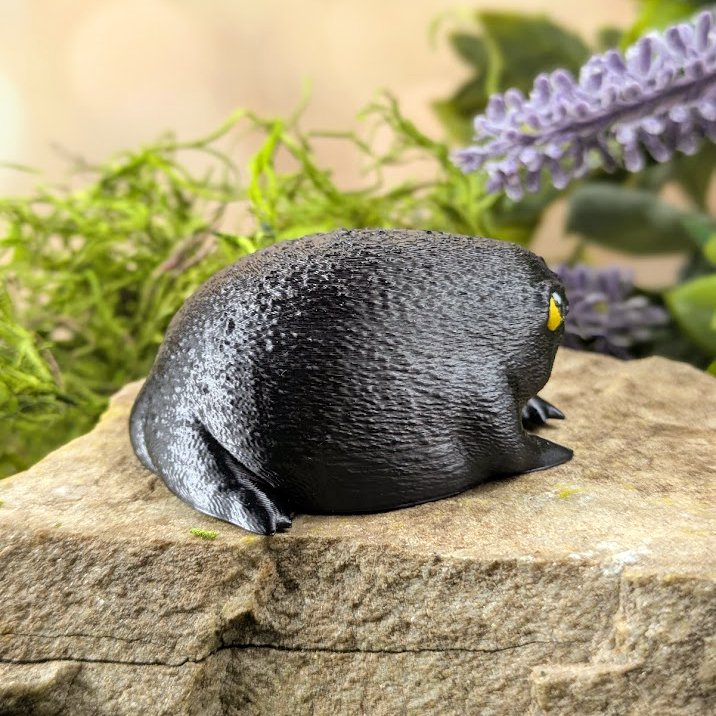 Right side view of the grumpy rainfrog figurine, its yellow eyes peeking slightly from the front.