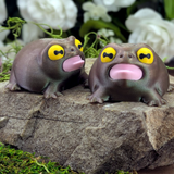Two Screaming Frog figurines side by side on a rock, both with yellow eyes and open pink mouths in a shouting pose.