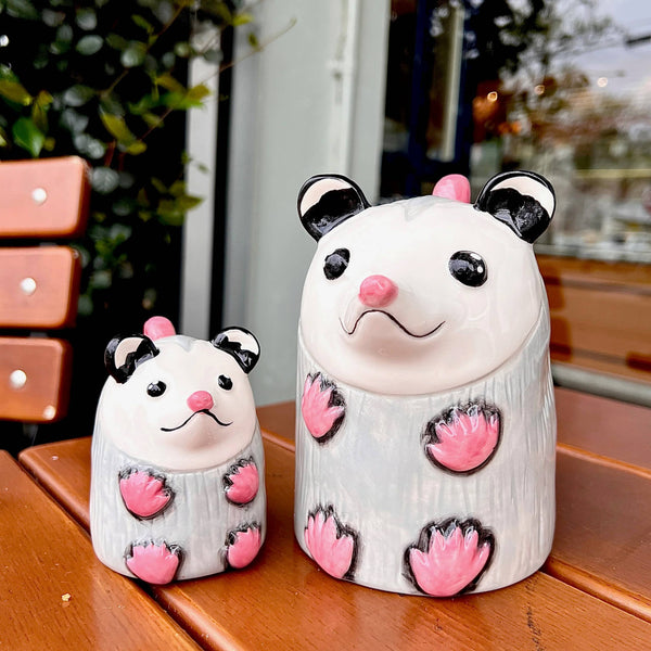 Two possum shaped coffee mugs sitting on a wooden surface.