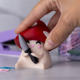 Mushroom figurine with a red cap and a knife held by a hand against a blurred background