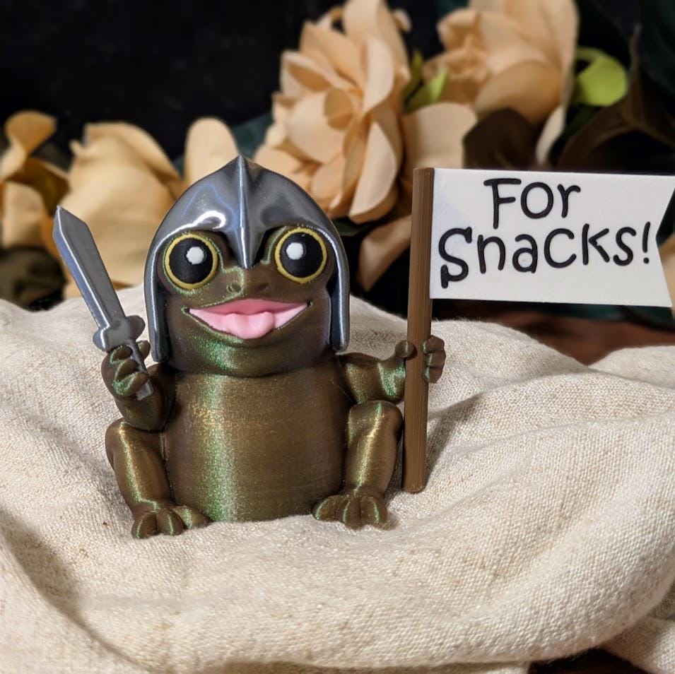 Sir Glorb™ seated on cloth surface, holding both sword and “For Snacks!” flag, with floral background.