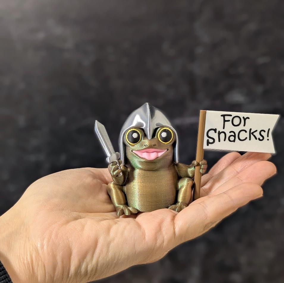 Sir Glorb™ shown in hand for scale, holding sword and “For Snacks!” flag with joyful expression.