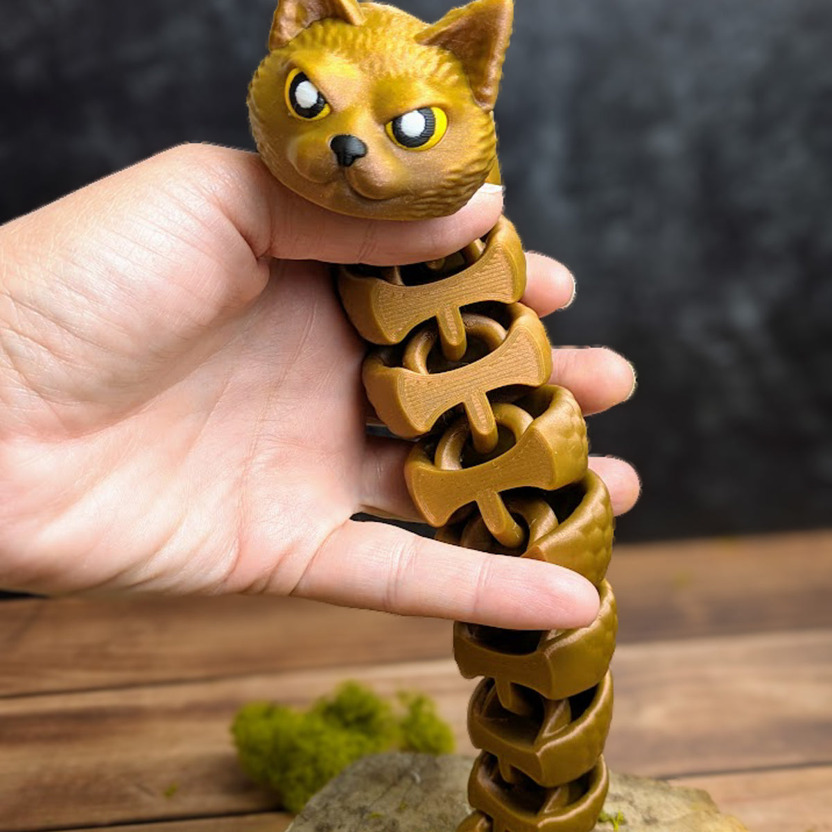 Vertical image of the Snat figurine stretched out while held in a hand, showcasing the full length of its flexible form and triangular tail.