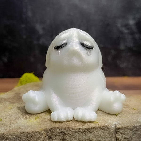 A Moonstone Tears squonk, glowing in ethereal sadness while sitting on a rock.