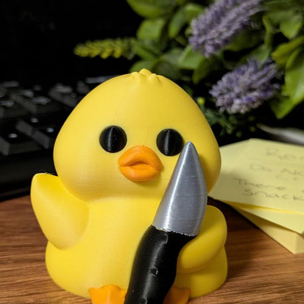 Stabby Duck sitting proudly with knife in hand, posed beside a stack of post it notes and leafy greens.