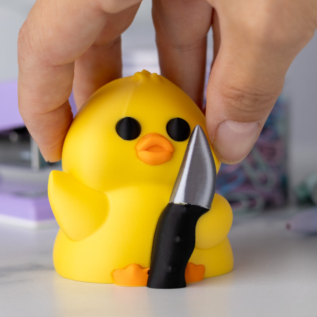 Yellow duck holding a knife with a blurred background with a hand for scale.