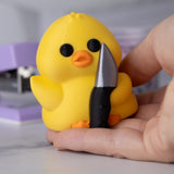Yellow duck holding a knife with a blurred background, held in a hand for scale.