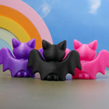 Back view of bat figurines with wings outstretched, pink, purple, and black bats