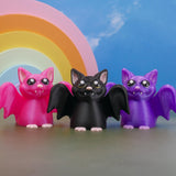 Spooky cute bat figurines posed under pastel rainbow backdrop