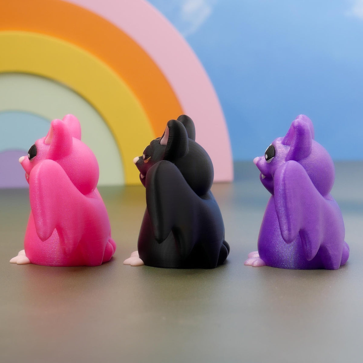 Side view of pink, black, and purple bat figurines lined up in a row