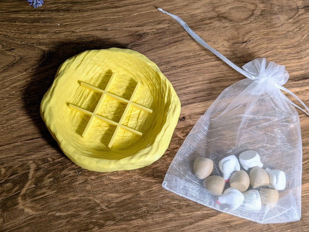 Yellow nest-shaped tic tac toe board beside a drawstring bag filled with chicken and egg pieces.