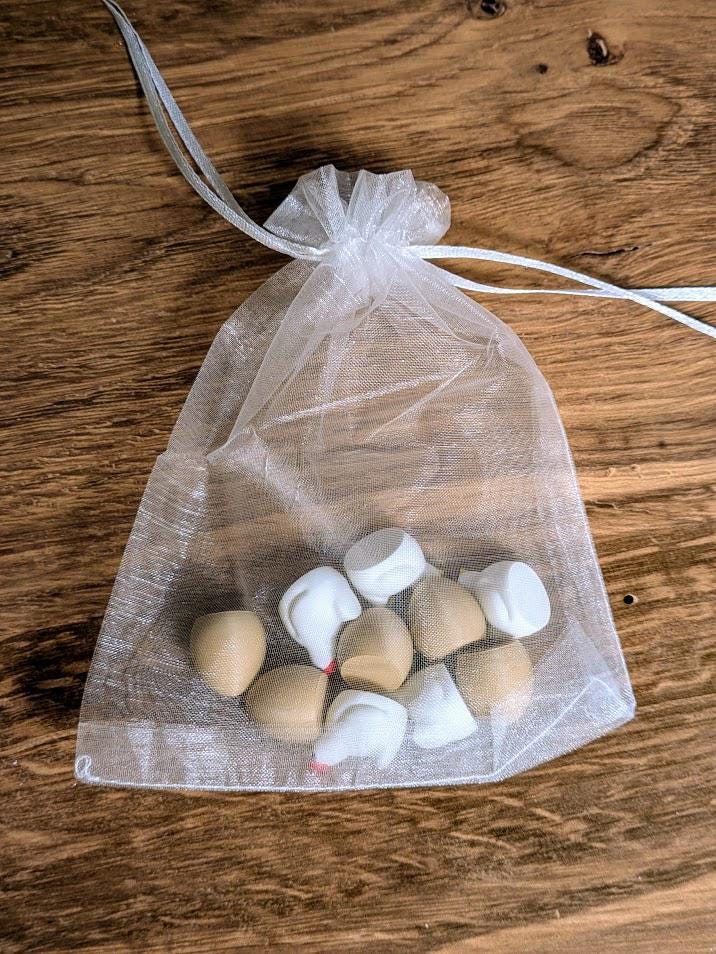 Transparent organza drawstring bag containing small chicken and egg pieces, resting on a rustic wooden table.