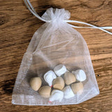 Transparent organza drawstring bag containing small chicken and egg pieces, resting on a rustic wooden table.